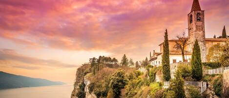 A historic building with a bell tower, situated on a cliff overlooking a body of water.