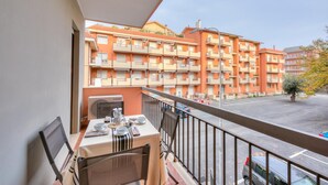 A balcony with a table set for dining, overlooking a parking area and a row of multi-story buildings.