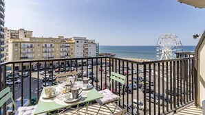 A balcony with a table set for dining, overlooking a parking lot and a Ferris wheel, with buildings and the sea in the background. - Bedo House Beach Front (Follonica)
