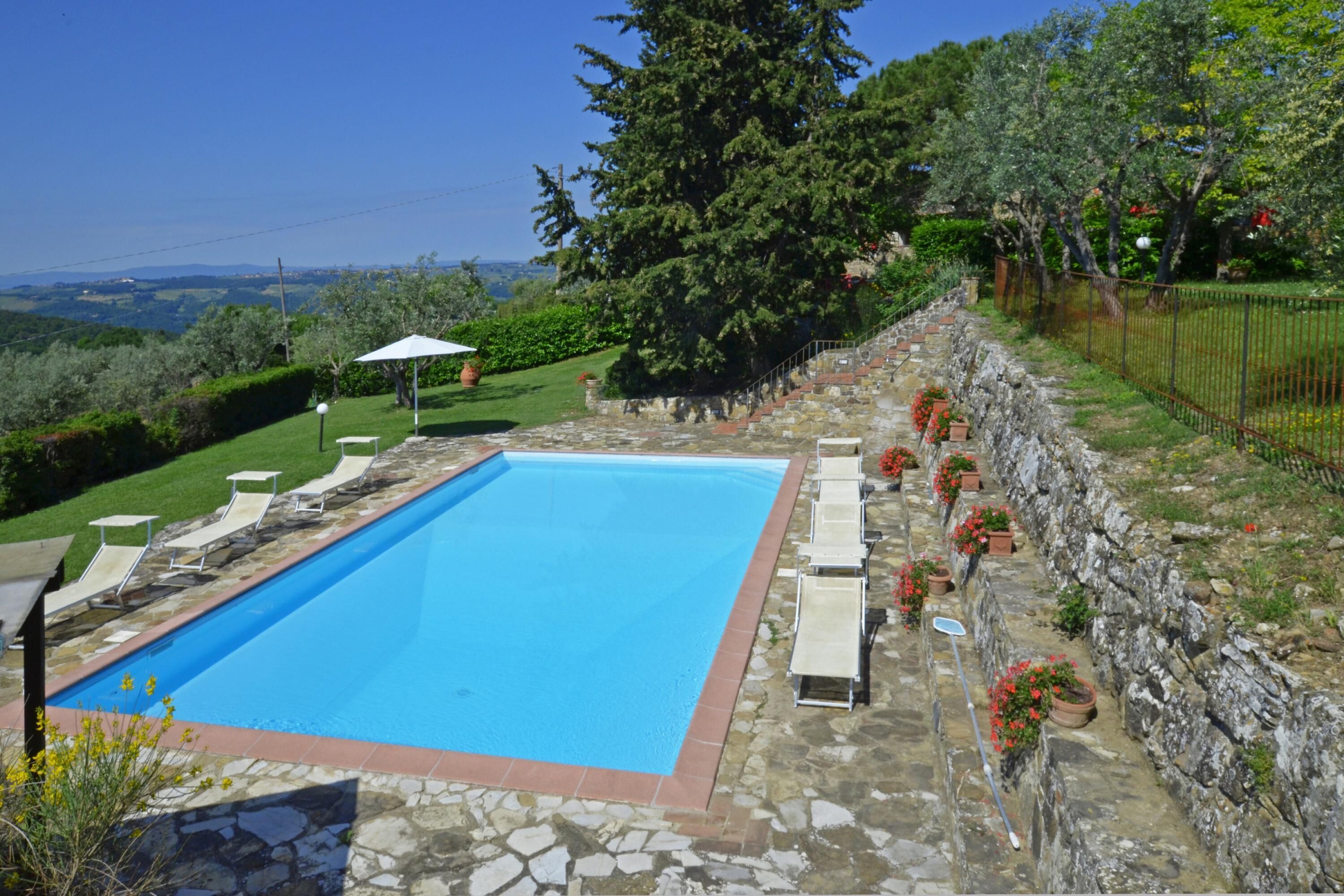 Une piscine rectangulaire bordée de pierres, entourée de chaises longues et de plantes en pot.