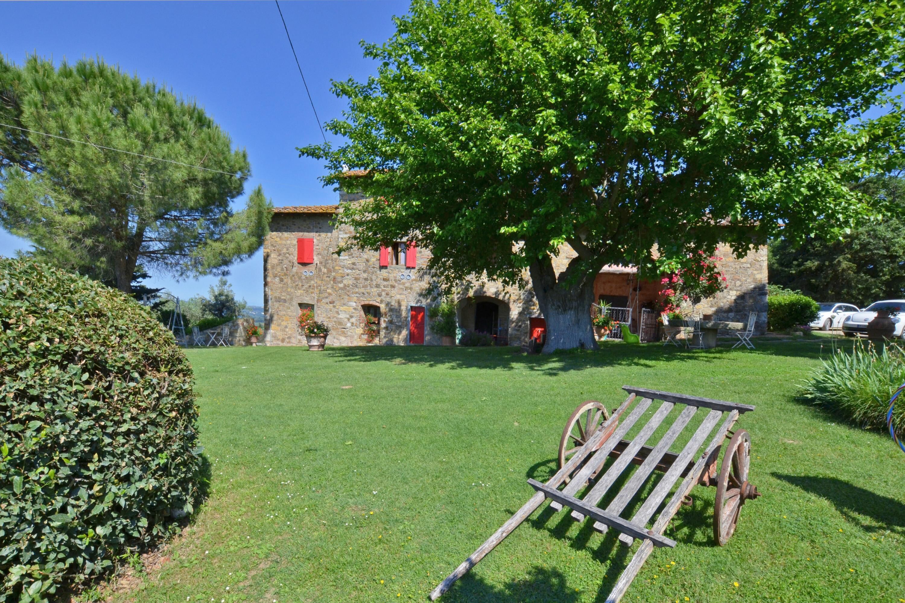 A stone building with red shutters, a wooden bench, and a large tree in front.