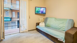 Sala de estar com sofá, televisão fixada na parede e porta de vidro deslizante para uma varanda externa.