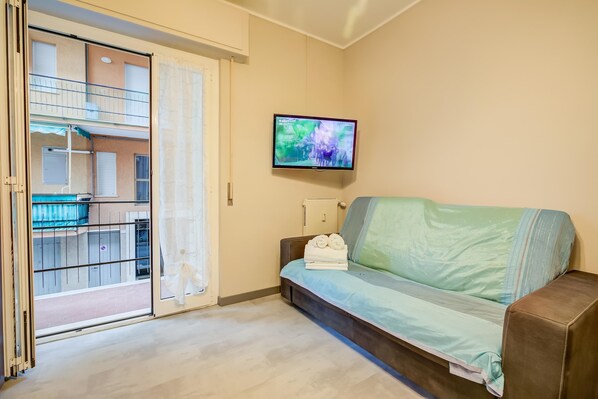 A living room with a sofa, a television mounted on the wall, and a sliding glass door leading to an outdoor balcony. - Sea Way - 150m From The Sea (Pietra Ligure)