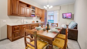 Cozinha moderna com armários de madeira, uma mesa de jantar para quatro pessoas e uma televisão na parede.