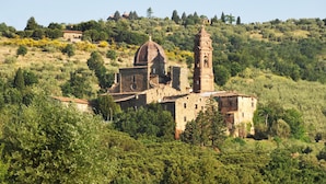 Um edifício histórico com uma torre de sino e cúpula, cercado por vegetação densa e colinas.