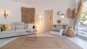 Un salon moderne avec un mur en briques blanches, un canapé, une table basse, une table d’appoint et une grande fenêtre donnant sur un beau paysage.