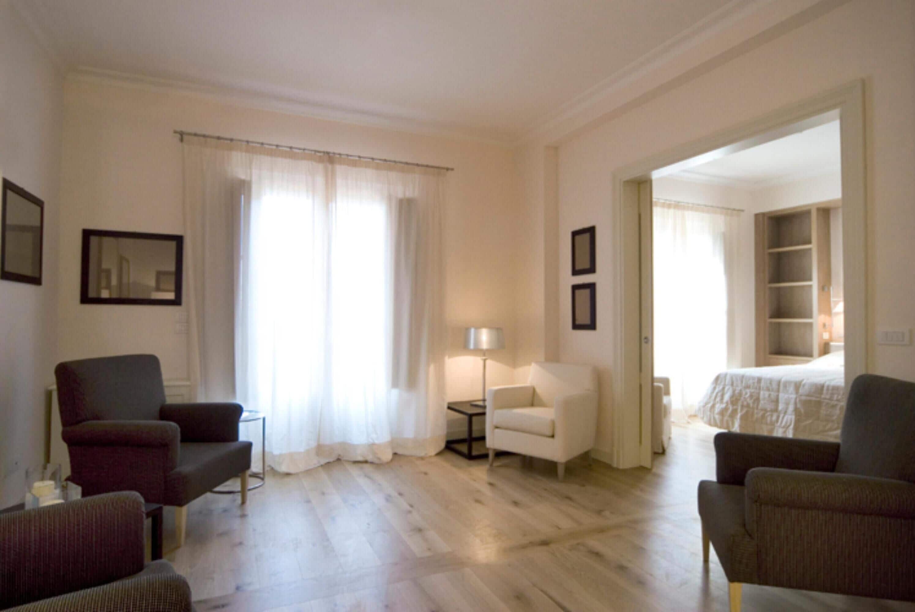 Camera d'albergo con un letto, due poltrone, un tavolino con una lampada e un'ampia finestra con tende.