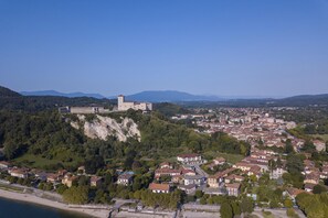 A coastal town with a prominent castle on a hill, surrounded by residential buildings and greenery. - Vista di Maccagno Fantastico Pool (Maccagno con Pino e Veddasca)