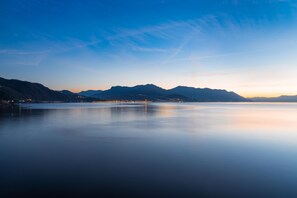 A calm lake with mountains in the background and a pier extending into the water. - Vista di Maccagno Fantastico Pool (Maccagno con Pino e Veddasca)