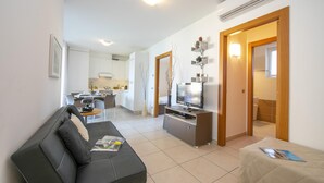 A modern living room with a black sofa, a TV on a wooden stand, and a dining area in the background.