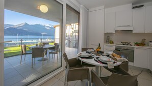 A dining area with a view of mountains and a lake, a kitchen with white cabinets, and a dining table set with plates and cutlery.