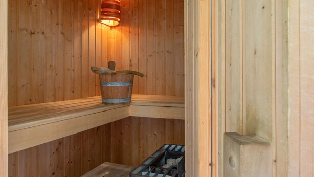 En træsauna med træbænk, spand og varmeovn.