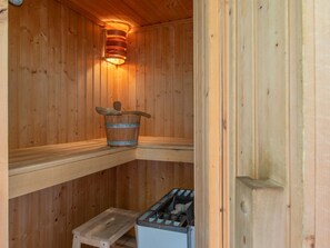 A wooden sauna with a wooden bench, a bucket, and a heater. - Villa in Zeeland Near the Beach (Scharendijke)