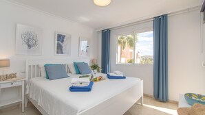 A modern bedroom with a large bed, a bedside table, a desk, and a window with curtains. - Family Duplex Riviera With Pool (Mijas)
