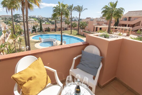 A balcony with a pool view, white chairs, and a table with wine glasses. - Family Duplex Riviera With Pool (Mijas)