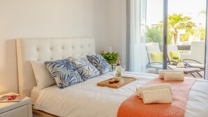 Une chambre d’hôtel avec un grand lit, un plateau en bois sur lequel se trouvent une bouteille et des verres, et une vue sur l’espace extérieur aménagé pour les clients.