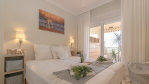 Ein Schlafzimmer mit Bett, zwei Nachttischen, einem Fenster mit Vorhängen, einem Balkon mit Pflanze und einem Bild an der Wand.