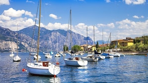 Un port de plaisance où sont amarrés de nombreux voiliers, avec des montagnes en arrière-plan et des bâtiments le long de la côte.
