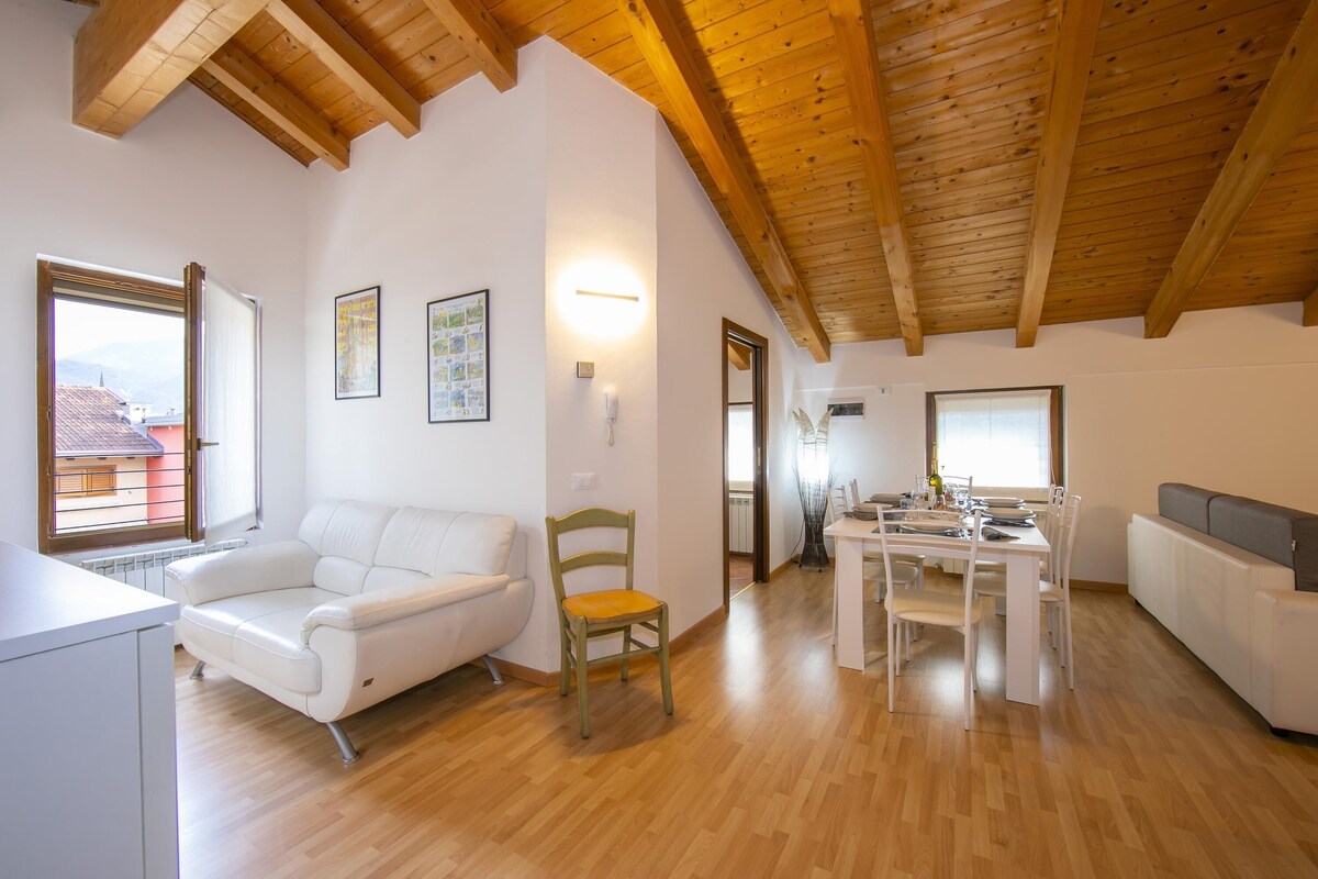 A spacious living area with a wooden ceiling, a white sofa, a dining table set, and a view through a large window.