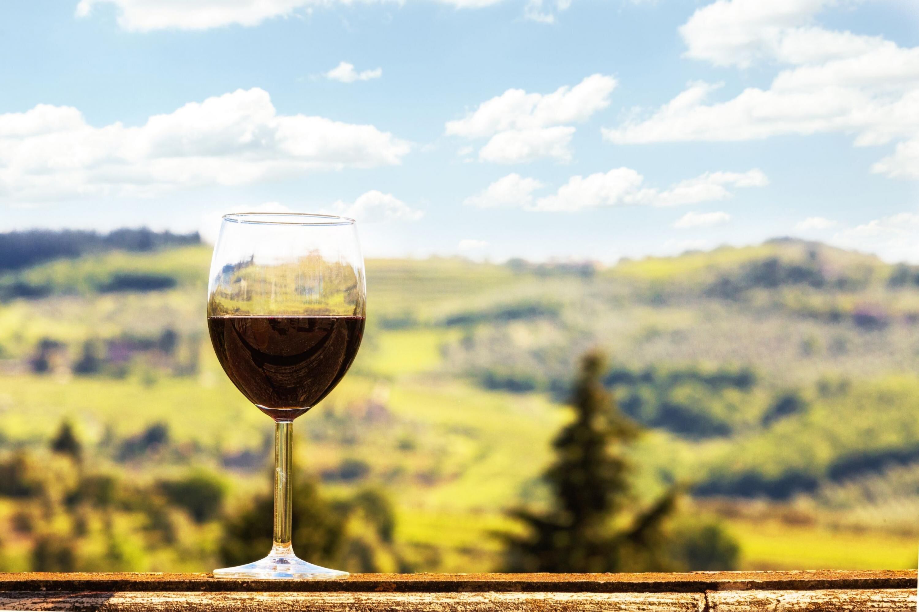 Um copo de vinho tinto sobre um parapeito de madeira, com uma paisagem desfocada ao fundo.