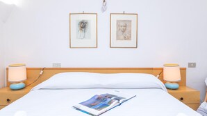 A neatly made bed with a magazine, two bedside lamps, and two framed artworks on the wall. - La Lampara House in Cannigione (Arzachena)