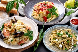 Tres platos de pasta con diferentes ingredientes, como camarones, mejillones y guisantes, acompañados de pan y un bol de salsa.