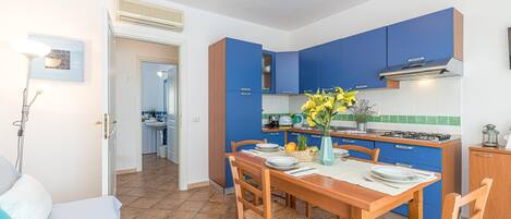 A modern kitchen with blue cabinets, a wooden dining table set for four, and a vase with flowers on the table.