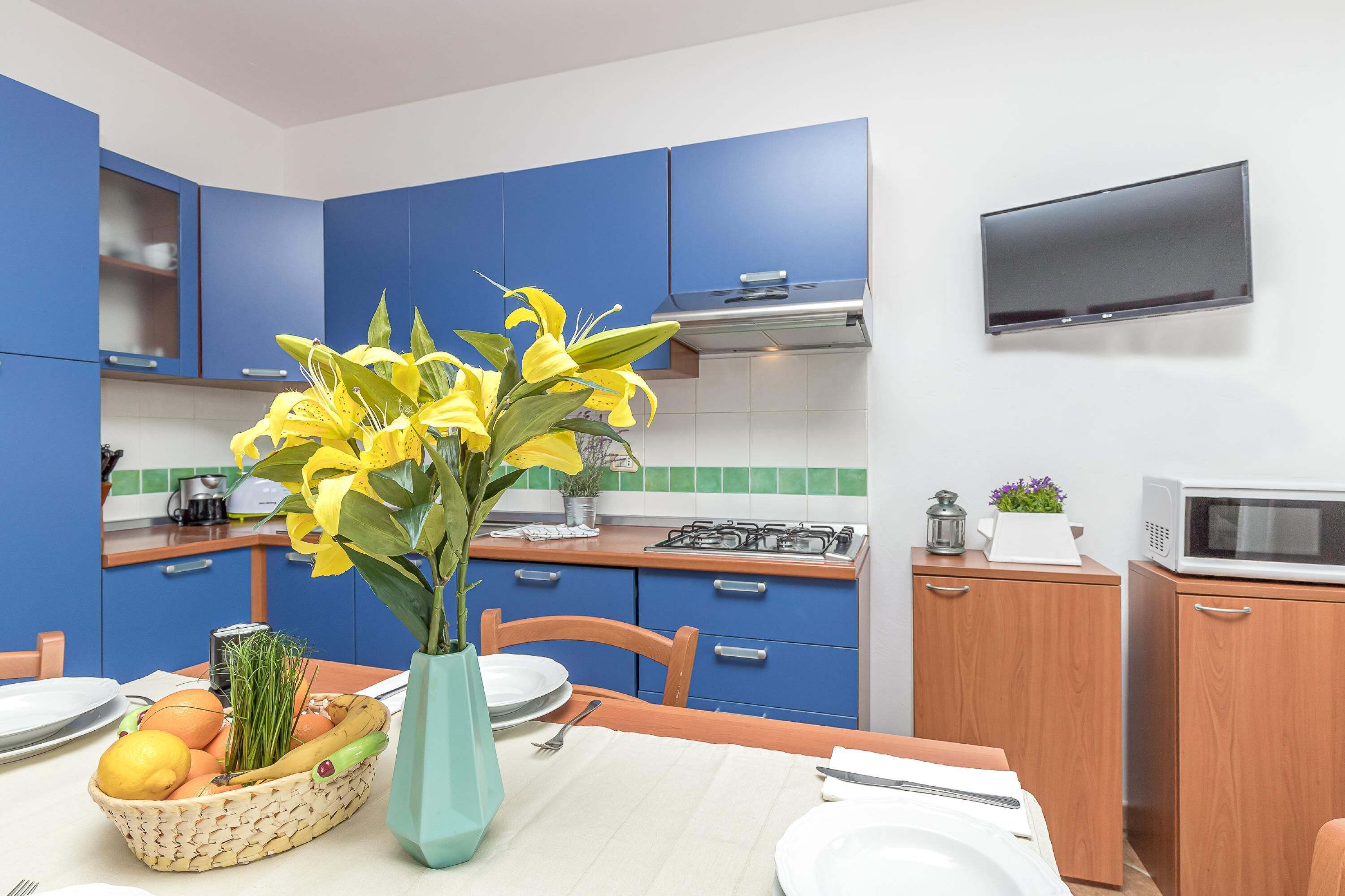 Una cucina moderna con mobili blu, un fornello a gas, un forno a microonde e un tavolo da pranzo apparecchiato con piatti e un cesto di frutta.