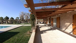 Un patio couvert avec une piscine, un sol en pierre et un bâtiment en briques doté de portes et de fenêtres en bois.