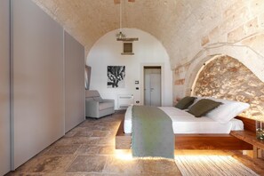 Une chambre avec un sol en pierre, un lit recouvert d’une couverture verte, un canapé et un tableau accroché au mur.