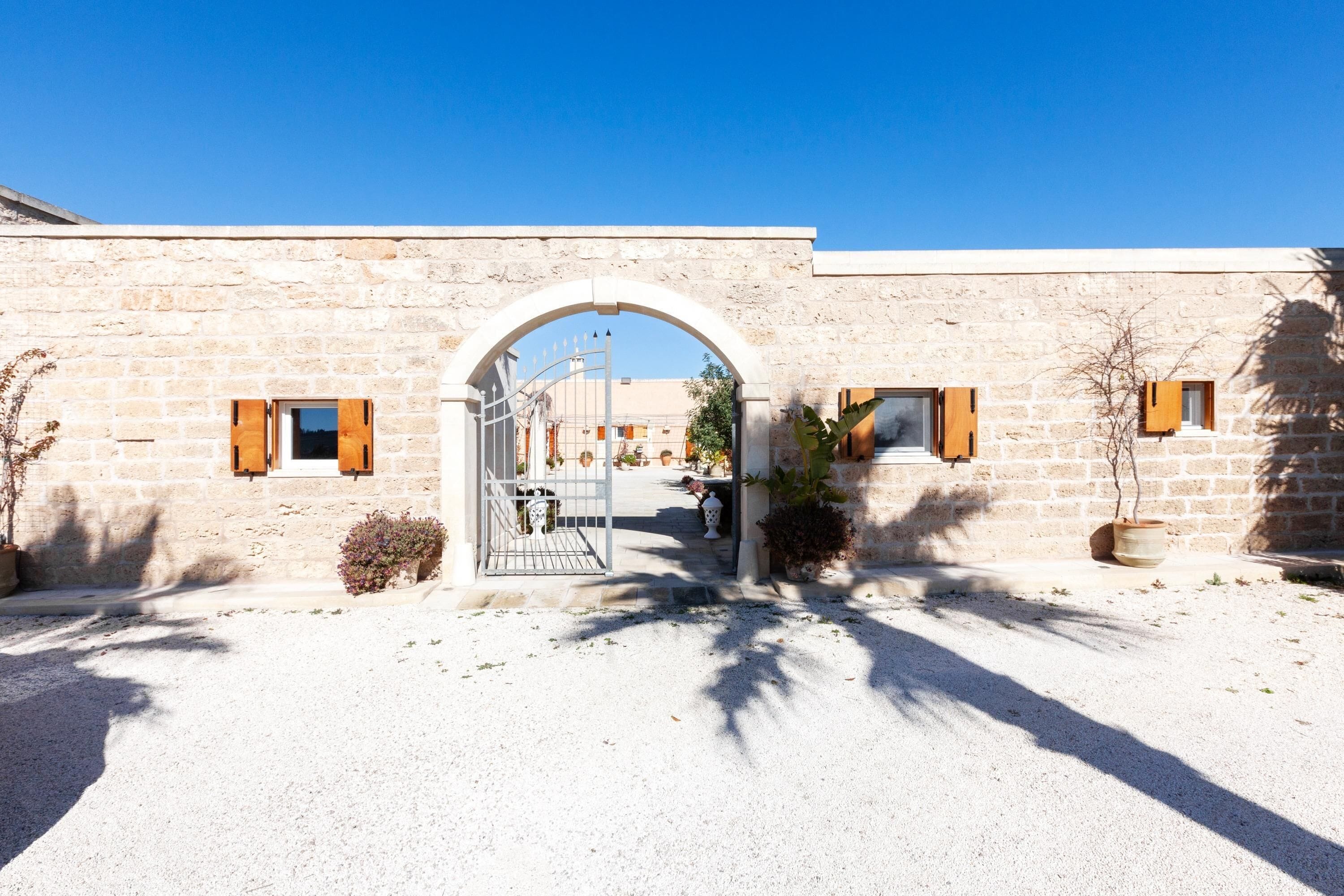 A stone building with a large arched entrance, potted plants, and a gravel driveway.