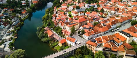 An aerial view of a town with a river, featuring a bridge, historic buildings with red roofs, and a prominent church tower.