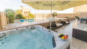Ein Whirlpool mit einem Coca-Cola Sonnenschirm, ein Pool, Sitzgelegenheiten im Freien und Blick auf historische Architektur.