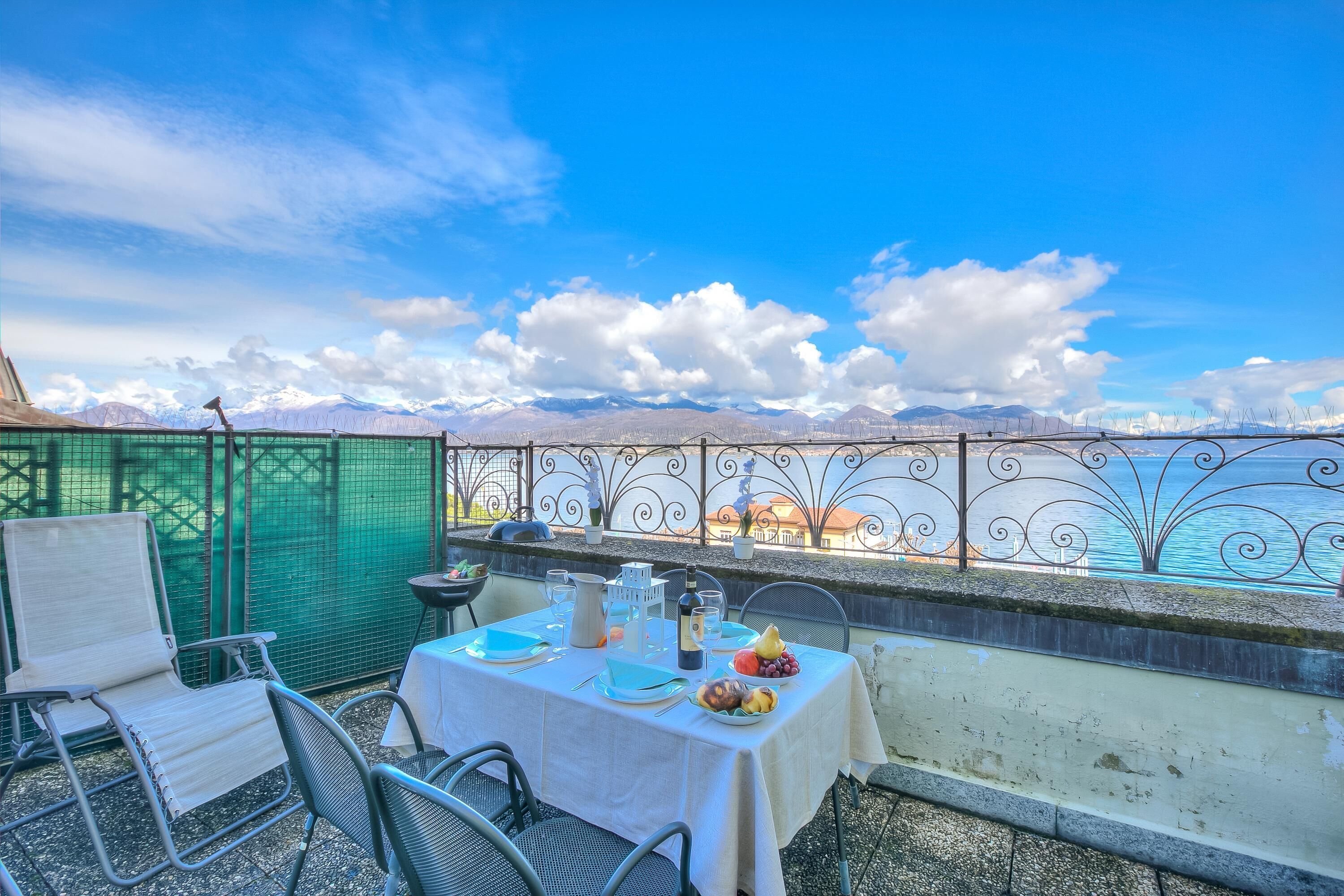 A terrace with a table set for two, overlooking a mountainous landscape and a body of water.
