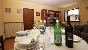 Une table à manger dressée avec des assiettes, des couverts et une bouteille de vin, entourée de chaises et agrémentée d’un vase de fleurs.