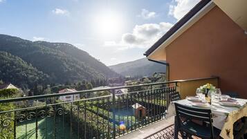 Un balcone con tavolo apparecchiato per mangiare, affacciato su una rigogliosa valle e montagne.