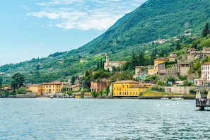 A coastal town with buildings along the waterfront, a church with a bell tower, and boats on the water. - Rosa Liano in Hilly Area (Gargnano)