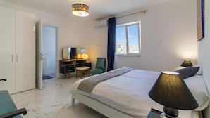 Ein modernes Hotelzimmer mit einem großen Bett, einem Schreibtisch mit Stuhl, einem Kleiderschrank und einem Fenster mit Vorhängen.