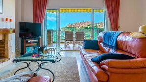 Un salon avec un canapé en cuir, une table basse en verre, un téléviseur et un balcon offrant une vue sur les immeubles.