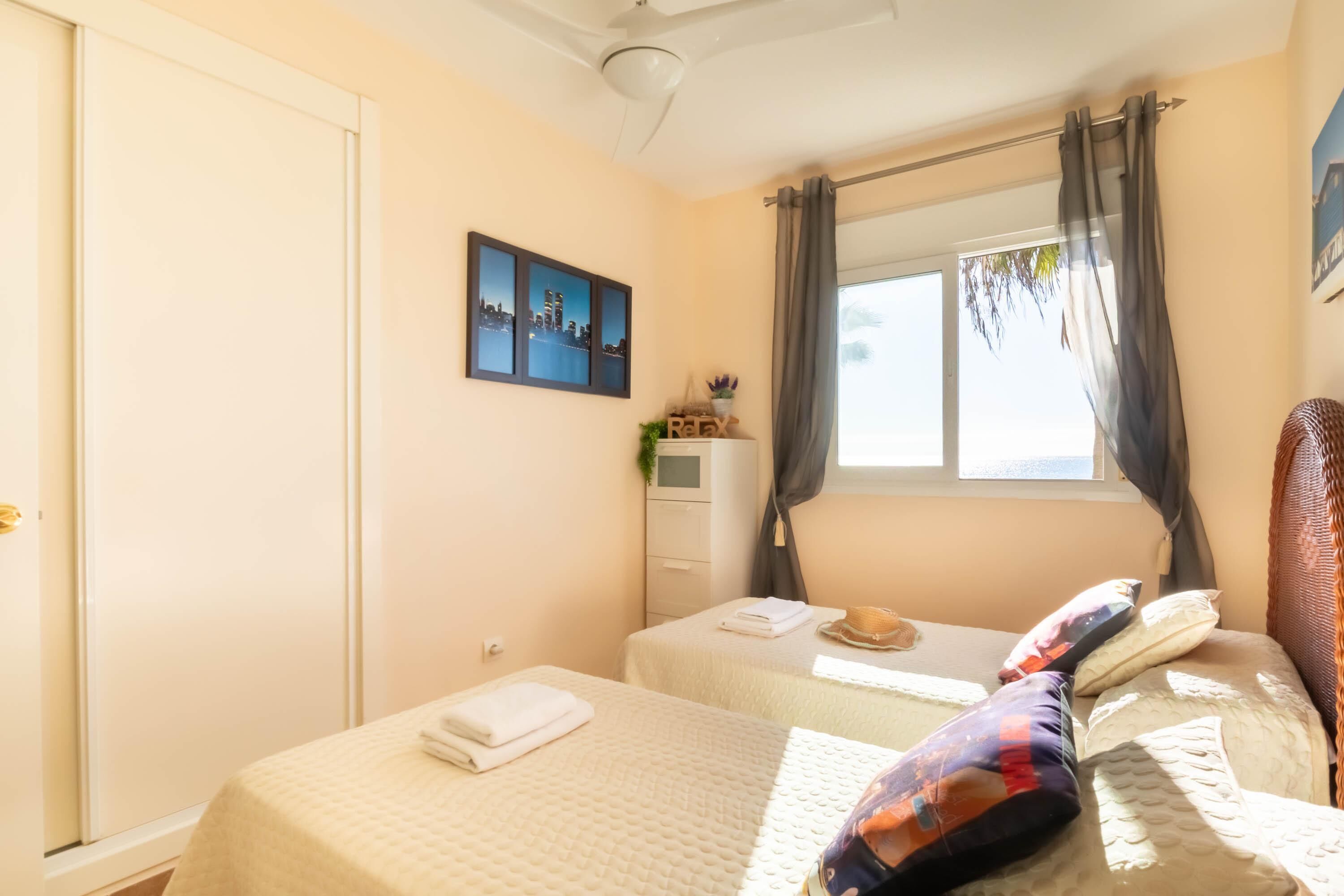 A hotel room with two beds, a window with curtains, a wall-mounted picture, and a ceiling fan.