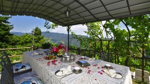 En uteservering med ett bord för två personer, omgiven av frodig grönska och en vacker utsikt över bergen.