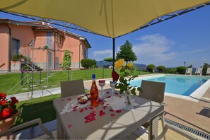 An outdoor patio with a table set for two, a pool, and a house in the background. - Villa Medicina in Medicina (Pescia)
