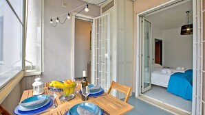 A dining area with a table set for two, a bowl of fruit, and a bottle of wine. A bedroom with a bed and blue bedding is visible through an open door. - Monopoli Beach House (Monopoli)