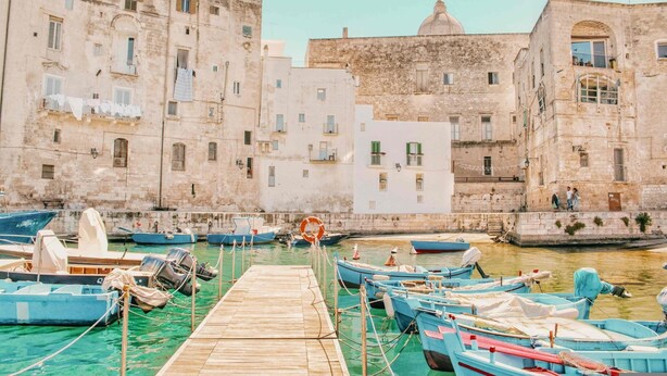 A waterfront with boats docked at a wooden pier, surrounded by historic stone buildings with balconies and windows. - Monopoli Beach House (Monopoli)