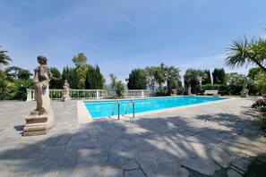 Μια πισίνα με ένα άγαλμα στο προσκήνιο, περιτριγυρισμένη από δέντρα και ένα μονοπάτι από πέτρα.