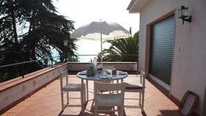 A round table with chairs on a balcony, an umbrella, and a view of trees and a building. - Paradiso Al Mare Shared Pool (Diano Marina)