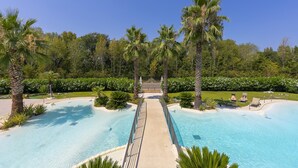 A swimming pool with a central walkway, surrounded by palm trees and lush greenery. - Rivoltella Apt With Pool 600m From Lake (Desenzano del Garda)