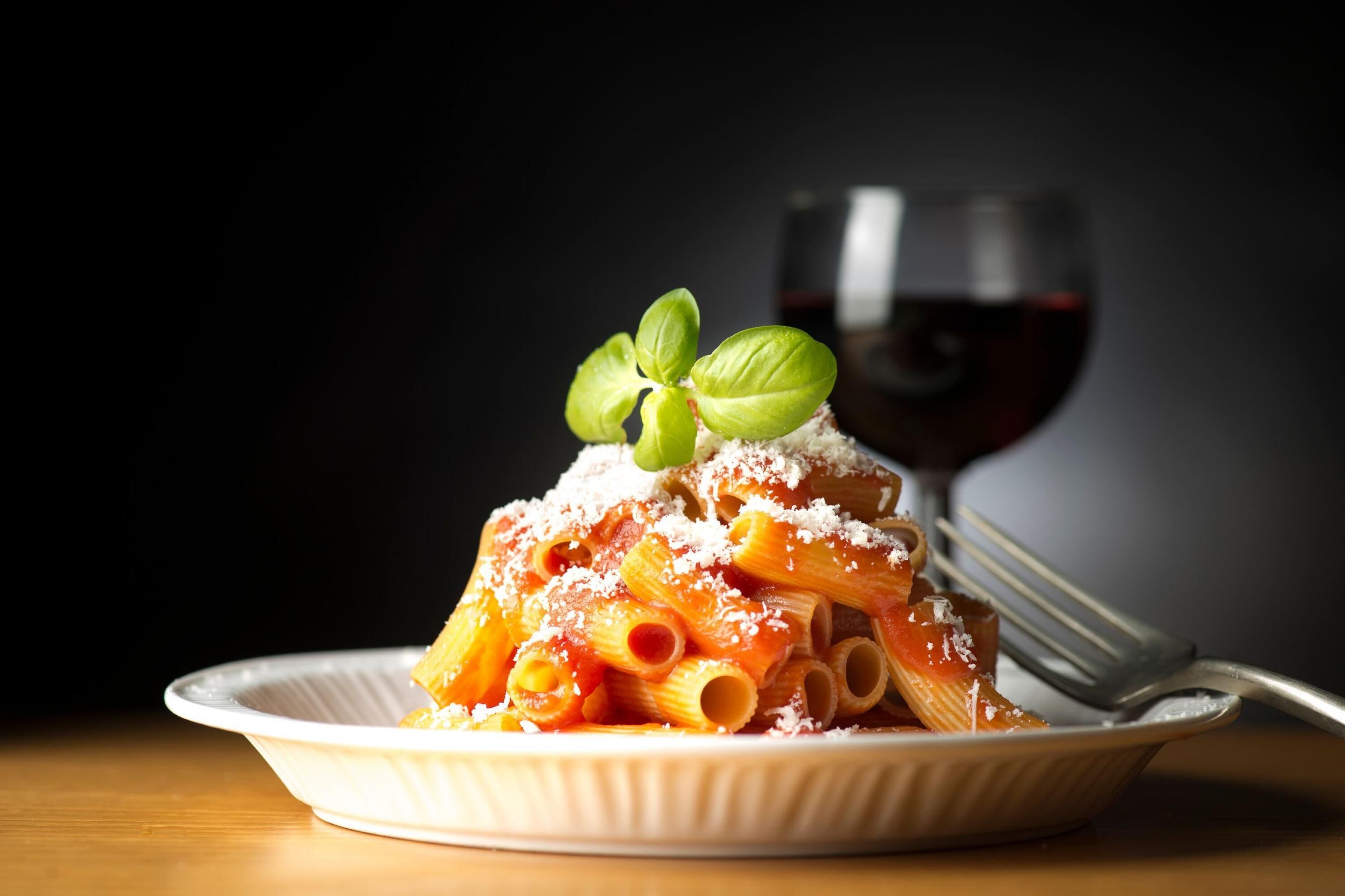 A plate of pasta with a glass of red wine in the background.