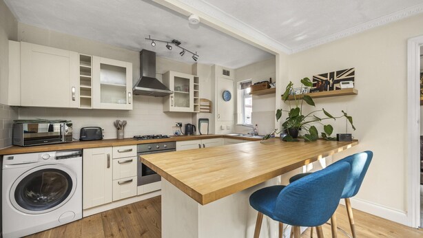 A modern kitchen with white cabinets, a wooden countertop, a washing machine, and a bar area with blue chairs. - Secret Garden House With Free Parking By My Getaways (Horsham)