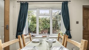 A dining table set with plates, cutlery, and glasses, positioned in front of a window with curtains. - Secret Garden House With Free Parking By My Getaways (Horsham)